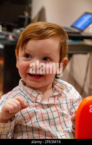 Portrait d'un bébé garçon mignon, à tête rouge, aux yeux bleus souriant et regardant l'appareil photo Banque D'Images