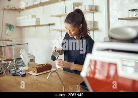 Jeune femme Barista versant du lait frais pour préparer du café latte pour le client dans le café. Pour la mise en route de petites entreprises dans l'industrie alimentaire concept Banque D'Images