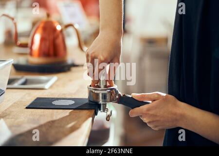 Barista tenant le porte-café en appuyant le café dans le porte-machine à café, gros plan Banque D'Images