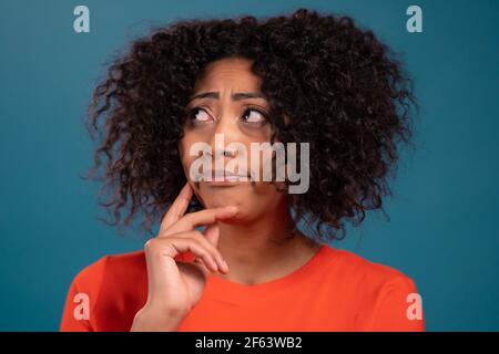 Je pense que la femme de course mixte regarde sur fond de studio bleu. Expressions de la face pensive. Joli modèle afro à l'apparence attrayante. Banque D'Images