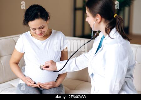 Concept De Grossesse En Sante Medecin Examinant La Femme Enceinte Heureuse Souriante De Race Mixte A L Ecoute Des Battements De Cœur De Bebe Tout En Etant Assis Sur Un Canape A La