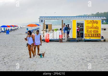 Deux touristes afro-américains portent un masque facial lorsqu’ils marchent avec leur chien après les locations de jet ski de Life’s a Beach sur la plage de Biloxi à Biloxi, Mississippi. Banque D'Images