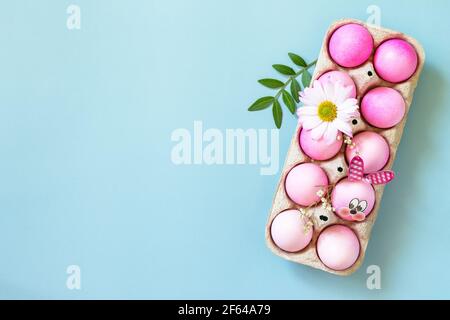 Concept de Pâques minimal. Ambiance printanière festive, boîte en papier avec œufs de Pâques dans les tons roses et fleur gerbera sur fond bleu pastel. Plan d'étapage avec vue de dessus. Banque D'Images