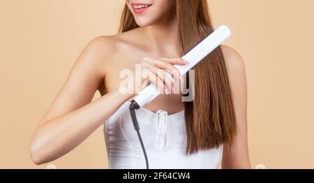 Bonne femme lissant ses cheveux avec un lisseur. Belle fille en utilisant la brosse coiffante sur ses cheveux brillants. Coiffure. Belle femme souriante repassage long Banque D'Images