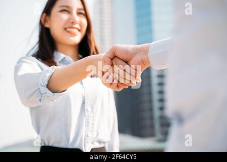 Gros plan des mains d'une jeune femme d'affaires asiatique souriante qui se secoue les mains avec un homme d'affaires en ville et un responsable de réunion pour un entretien Banque D'Images