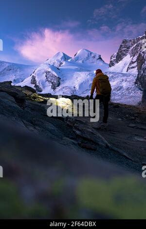 Mountaineer avec lampe frontale en admirant les sommets enneigés de Castor et Pollux à l'aube, Zermatt, canton du Valais, Suisse Banque D'Images