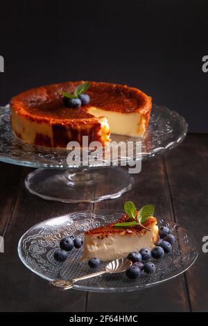 Cheesecake basque maison brûlé avec fromage à la crème, œufs et crème cuits dans une croûte de miettes. Une tranche de cheesecake sur une assiette de myrtilles et de menthe Banque D'Images