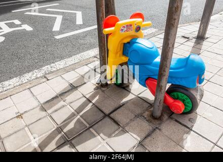 Vélo en plastique pour enfants verrouillé avec un cadenas en U pour service intensif poteau de parc à vélo à l'extérieur de l'école junior Banque D'Images