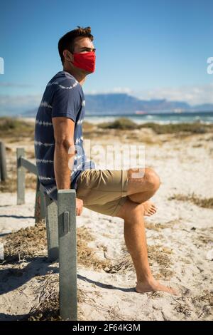 Homme caucasien portant des masques de visage assis sur la plage près de la mer Banque D'Images