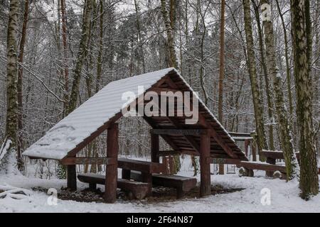 Aire de repos en forêt d'hiver pour les touristes, les voyageurs, abri en bois avec banc, table et toit recouvert de neige Banque D'Images