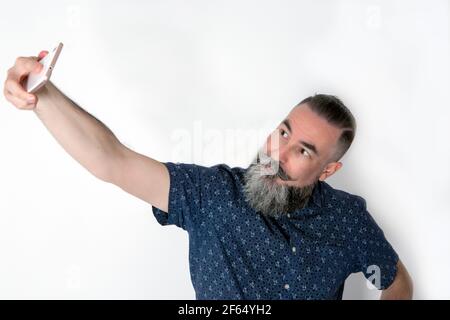 homme de 40 à 45 ans avec une grande barbe gris moyen utilisant son smartphone pour réaliser un autoportrait (sefie) Banque D'Images