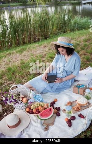 Une femme en chapeau de paille s'assoit sur un pique-nique un parc sur les rives d'une rivière Banque D'Images