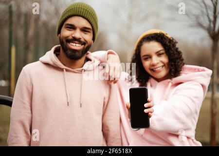 happy african american sportswoman montrant un smartphone avec écran vide près d'un ami souriant, arrière-plan flou Banque D'Images