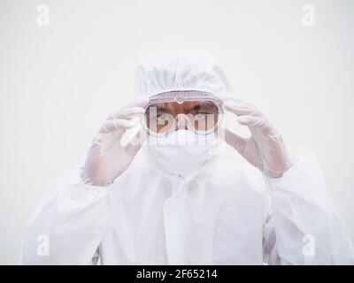 Gros plan de jeunes médecins ou scientifiques asiatiques en EPI suite uniforme tenant des lunettes avec les deux mains tout en regardant vers l'avant. Coronavirus ou COVID-19 concept i Banque D'Images