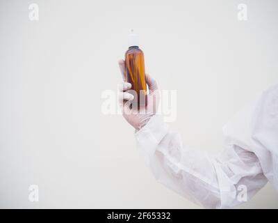 Portrait d'un médecin ou d'un scientifique dans un uniforme de la suite PPE tenant une bouteille en plastique avec un produit de soin de la peau. COVID-19 concept fond blanc isolé Banque D'Images