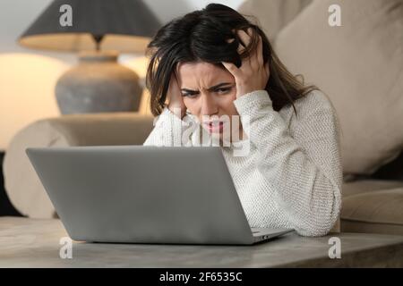Femme désespérée vérifiant les mauvaises nouvelles sur ordinateur portable dans la vie chambre à la maison Banque D'Images