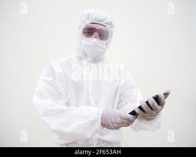 Jeune médecin ou scientifique dans l'uniforme de la suite PPE tout en jouant son téléphone pour discuter avec la famille ou freind et regardant la caméra. Coronavirus ou COVID Banque D'Images