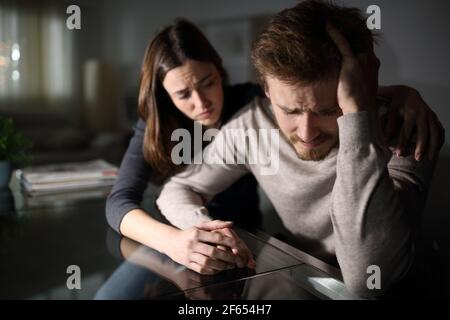 Triste homme étant réconforté par sa femme dans la nuit à la maison Banque D'Images