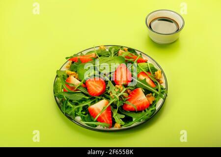 Salade de fraises d'été avec feuilles d'épinards, arugula, noix et vinaigre balsamique et sauce à l'huile d'olive sur fond vert avocat. Alimentation saine co Banque D'Images