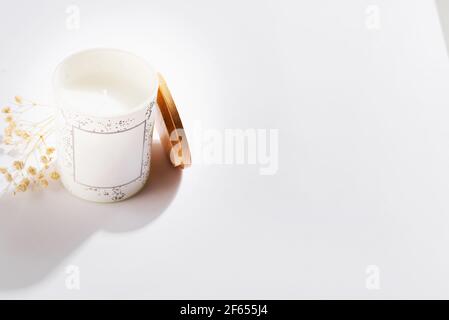 Bougies de soja en bouteilles de verre blanc avec couvercle et fleur sèche, sur fond blanc. Banque D'Images
