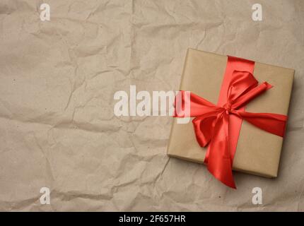 boîte en carton marron attachée avec un ruban rouge soie sur fond de papier marron, vue du dessus, gros plan Banque D'Images