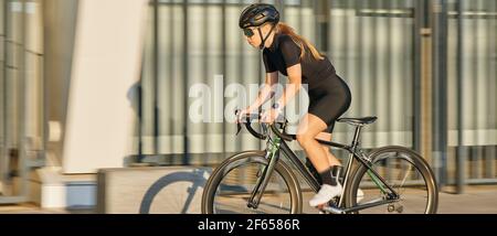 En-tête de site Web de vue latérale de cycliste professionnelle femme en noir vêtements de cyclisme et équipement de protection à vélo de la ville, se précipitant et passant Banque D'Images