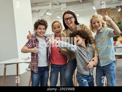 Nous sommes les meilleurs. Une équipe d'école heureuse composée de quatre jeunes élèves et de leur sympathique enseignante se posant ensemble, debout dans la salle de classe Banque D'Images