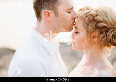Le marié embrasse doucement la mariée sur le front sur les rochers au bord de la mer, en gros plan Banque D'Images