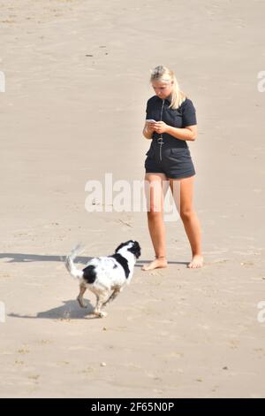 Jeune femme utilisant un téléphone mobile à l'extérieur, sur une plage, avec un chien, pendant la vague de chaleur de mars 2021, Bournemouth. Banque D'Images