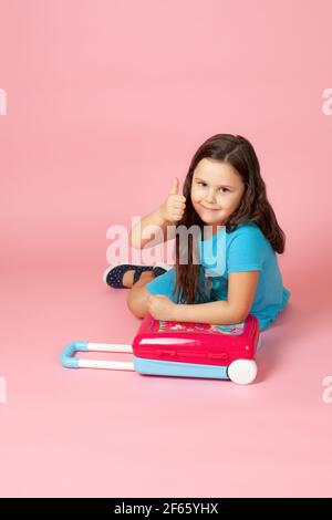 portrait d'une fille dans une robe bleue assise sur le sol avec ses mains sur un cramoisi en plastique et de donner un pouce vers le haut Banque D'Images