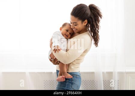 Une mère africaine aimante tenant bébé tout-petit dans les bras debout à l'intérieur
