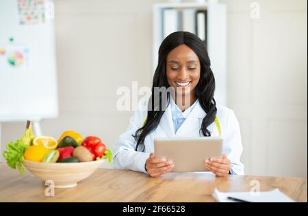 Nutritionniste afro-américain travaillant avec un ordinateur de tablette, donnant consultation en ligne au bureau médical, l'espace de copie Banque D'Images