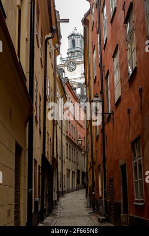 Une petite rue sinueuse à Gamla Stan, Stockholm, Suède, avec des bâtiments colorés de chaque côté et la tour de Storkyrkan visible au-delà. Banque D'Images