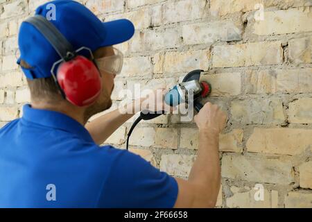 l'employé nettoie le vieux mur de briques à l'aide d'une brosse métallique rotative Banque D'Images