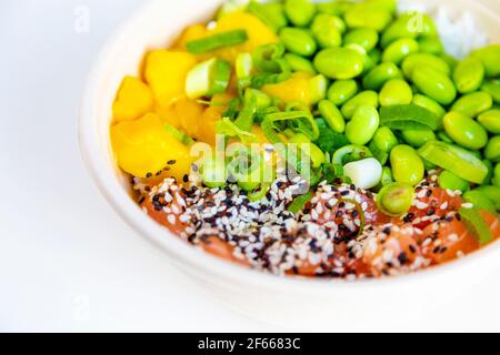 Un bol à poke avec de l'edamame, du saumon, de la mangue, recouvert d'oignons de printemps et de sésame sur un lit de riz Banque D'Images