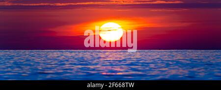 Grand soleil sur la mer pendant un coucher de soleil avec le ciel de couleur orange et la lumière se reflétant sur l'eau. Banque D'Images