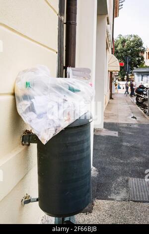 Poubelle noire sur le fond de la rue avec un sac de déchets. Une poubelle débordante contre un mur de briques. La surabondance de plastique et Banque D'Images