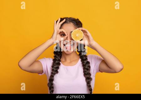 Femme indienne souriant, regardant la caméra à travers les doigts et les fruits Banque D'Images
