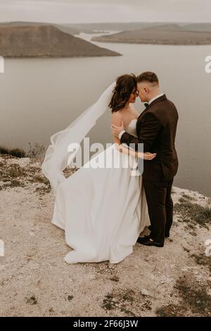 couple amoureux mariage newlyweds plein air. mariée en robe blanche voile long et marié en costume promenade en été automne sur la montagne au-dessus de la rivière. lever du soleil. homme Banque D'Images