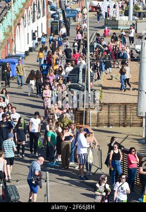 Brighton Royaume-Uni 30 mars 2021 - la file d'attente pour les toilettes publiques s'étend le long du front de mer de Brighton tandis que les visiteurs affluent vers le bord de mer le jour le plus chaud de l'année jusqu'à présent avec des températures atteignant le milieu des 20 centigrades dans certaines parties du Sud-est : Credit Simon Dack / Alamy Live News Banque D'Images