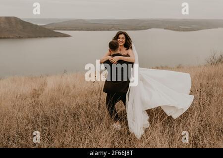 couple amoureux mariage newlyweds en blanc robe voile chaussures de sport en été, vous pourrez également profiter d'un tourbillon embrassant sur de grandes herbes terrain sur la montagne au-dessus de la rivière Banque D'Images