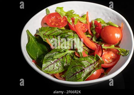 Salade végétarienne de tomates cerises, d'épinards, d'oignons rouges et de poivrons au beurre. Sur fond noir. Copier l'espace. Banque D'Images