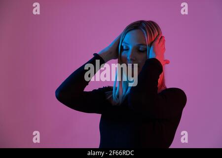 jeune femme blonde éclairée par des néons souffre de maux de tête et stress Banque D'Images