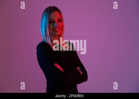 jeune femme blonde éclairée par des lumières néon regarde le appareil photo Banque D'Images