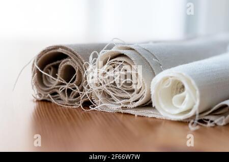 Trois rouleaux de linge naturel de différentes couleurs avec fils saillants sur une table en bois. Mise au point sélective. Vue en gros plan. Arrière-plan flou Banque D'Images