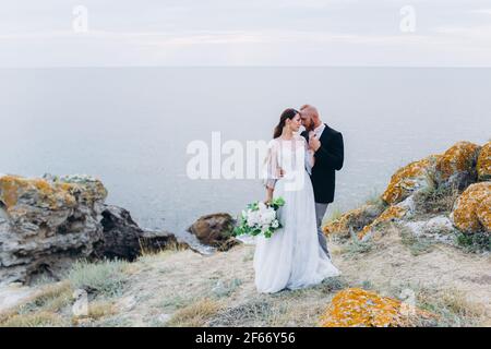 La mariée et le marié embrassant et embrassant sur le fond de la mer et des rochers. Banque D'Images