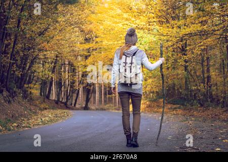 Femme randonnée sur la route en forêt d'automne. Tourisme avec sac à dos sur la route au milieu des bois. Voyager seul Banque D'Images