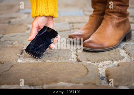 Une femme prend son téléphone intelligent cassé sur le trottoir. Écran tactile fissuré sur le téléphone portable. Téléphone cellulaire endommagé Banque D'Images