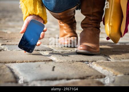 Femme qui prend un smartphone cassé avec un écran tactile fissuré dans la rue. Écran fragile endommagé sur le téléphone portable. Banque D'Images