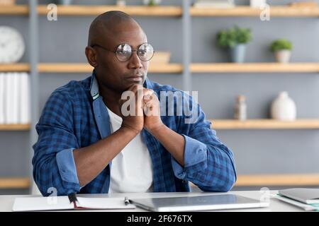 Réflexion sur le plan d'affaires. Entrepreneur noir réfléchi travaillant sur un nouveau projet au bureau à domicile Banque D'Images
